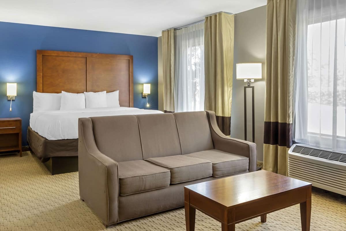 A hotel room with a bed, a sofa, a table, a nightstand, and a window with curtains.
