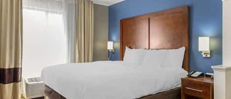 Ein Hotelzimmer mit einem großen Bett, einem Nachttisch mit Telefon und einem Fenster mit Vorhängen.