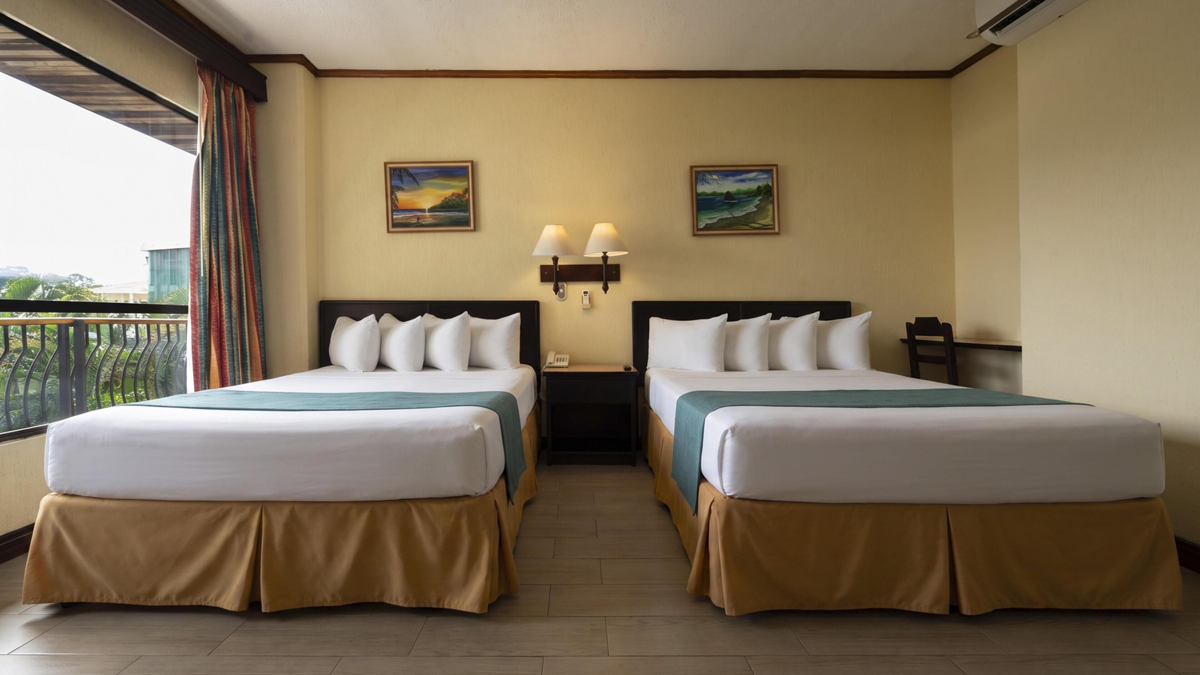A hotel room with two beds, a balcony, and two wall-mounted lamps.