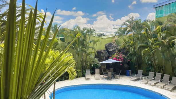 A swimming pool surrounded by lounge chairs and palm trees, with a view of a building in the background. - Best Western Hotel & Casino Kamuk (Quepos)