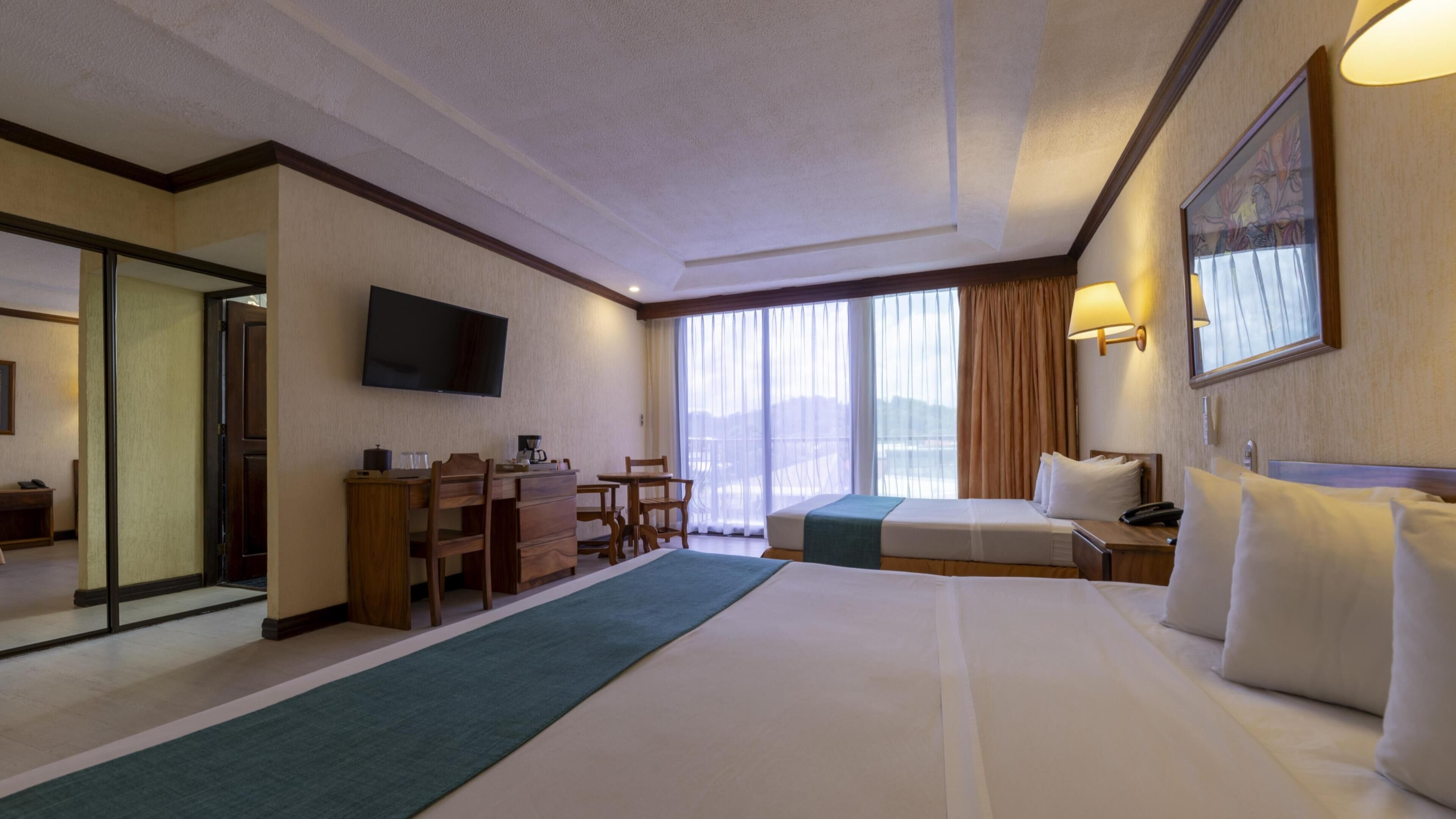 Una habitación de hotel con una cama grande, un escritorio con silla, televisión y ventana con cortinas.