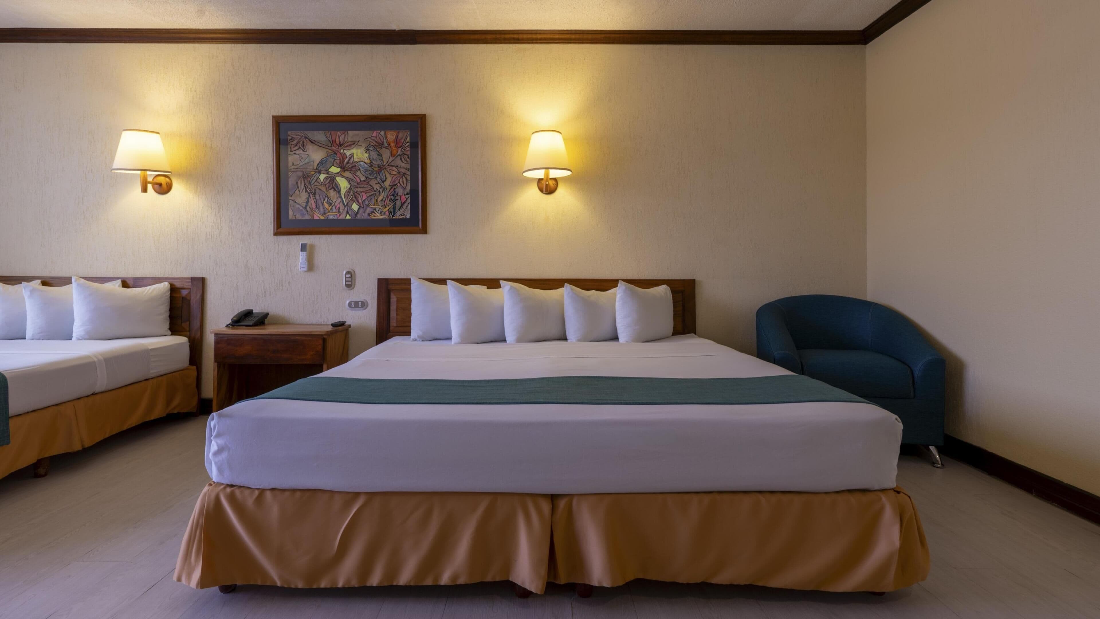 A hotel room with two beds, a desk, a chair, and two wall-mounted lamps.