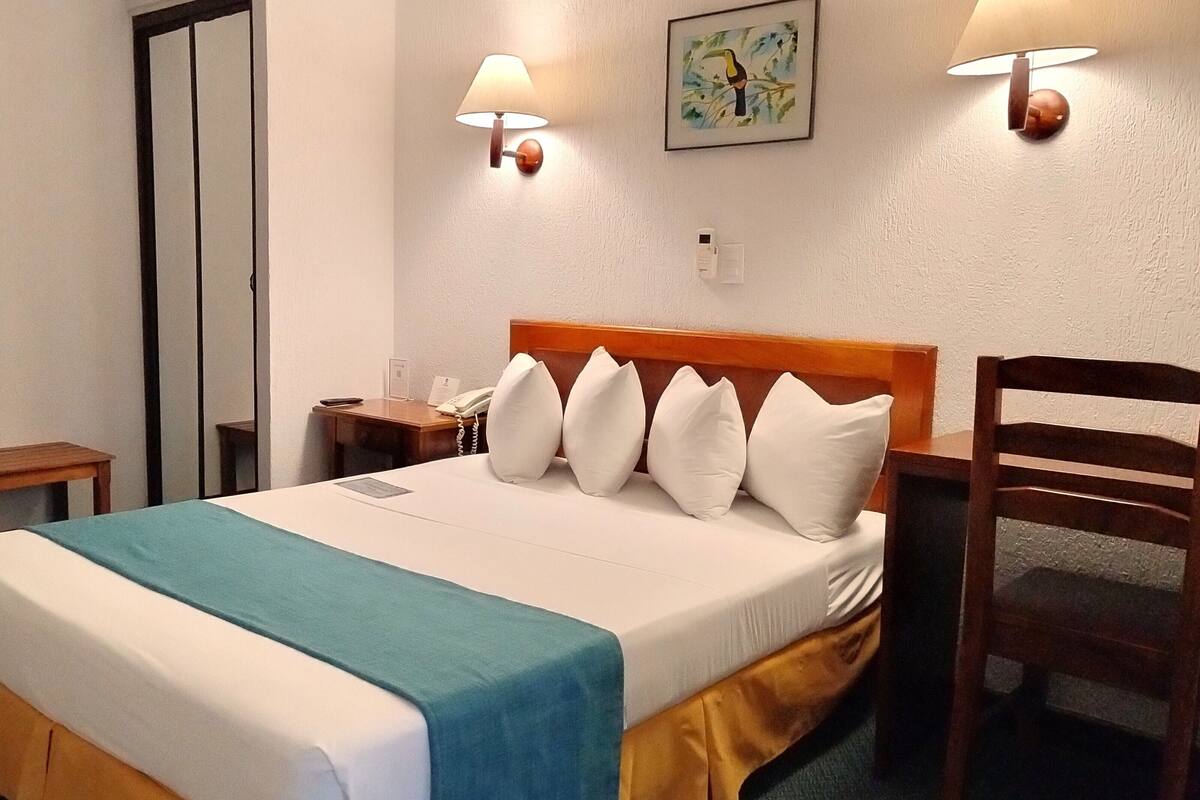 Ein Hotelzimmer mit einem Bett, einem Nachttisch, einem Sessel und einer Wandlampe.