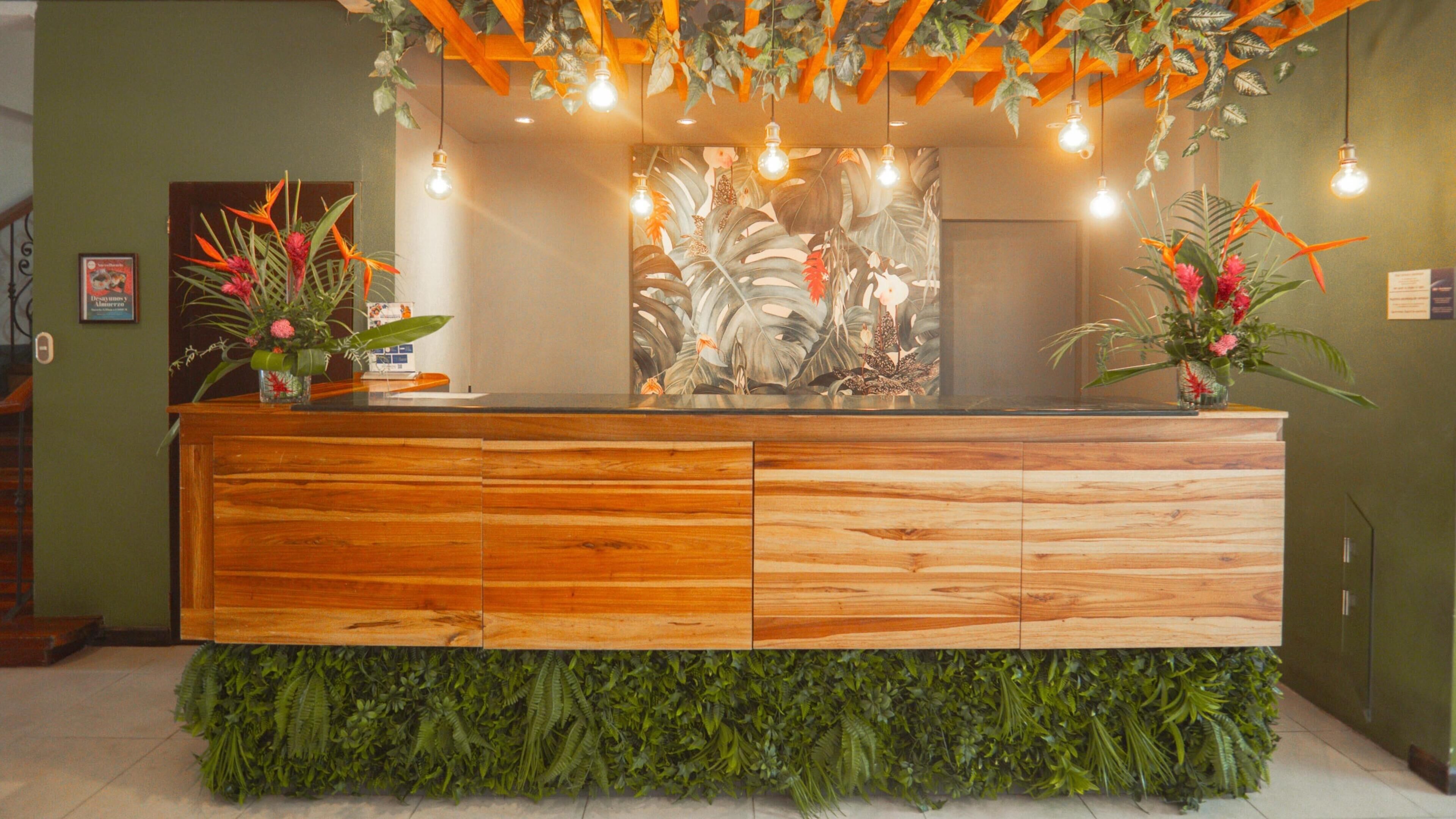 Un mostrador de recepción con detalles de madera y follaje verde en la base.