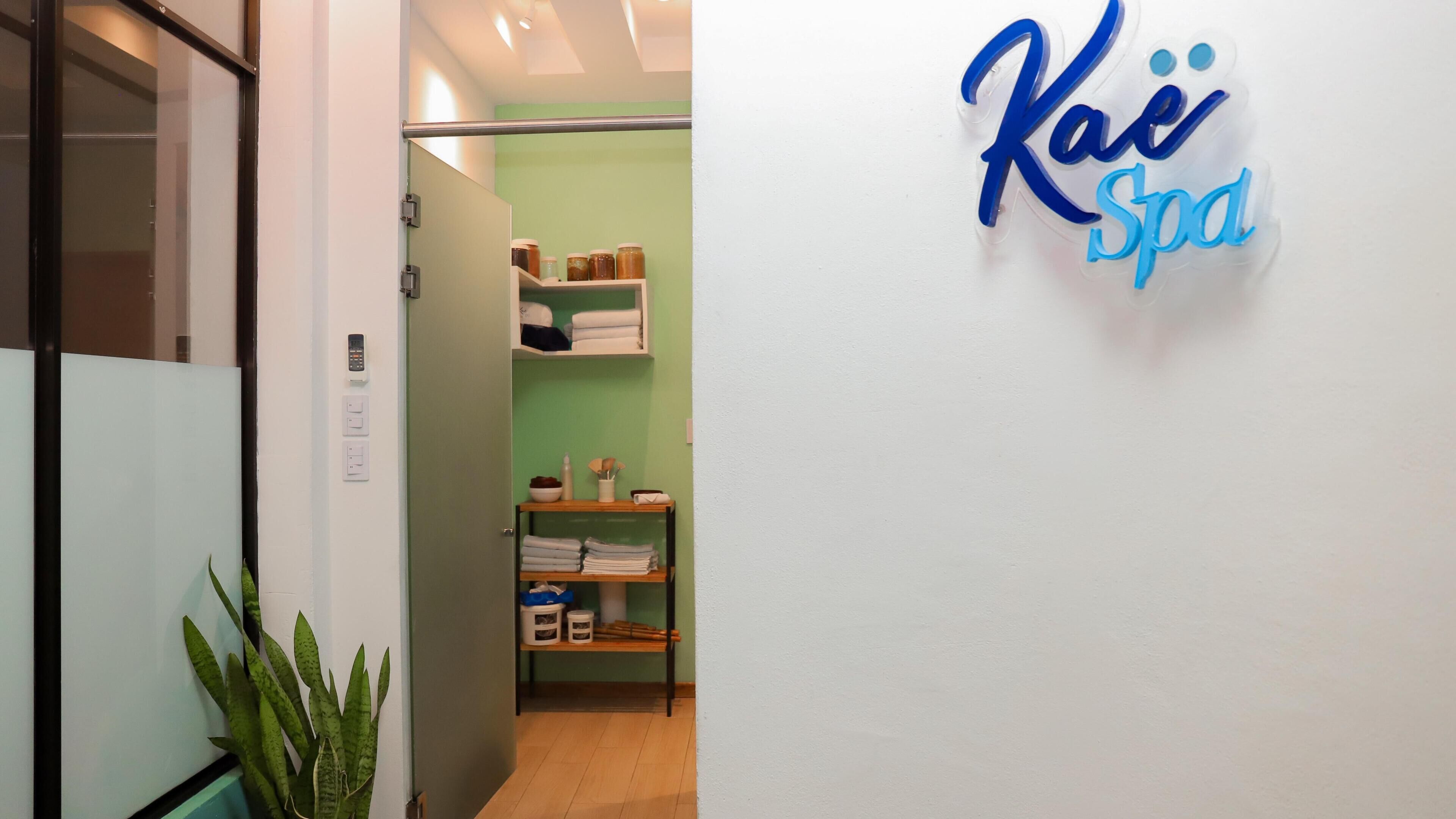 Un couloir avec un comptoir d’accueil, une plante et une enseigne murale indiquant « Kae Spa ».