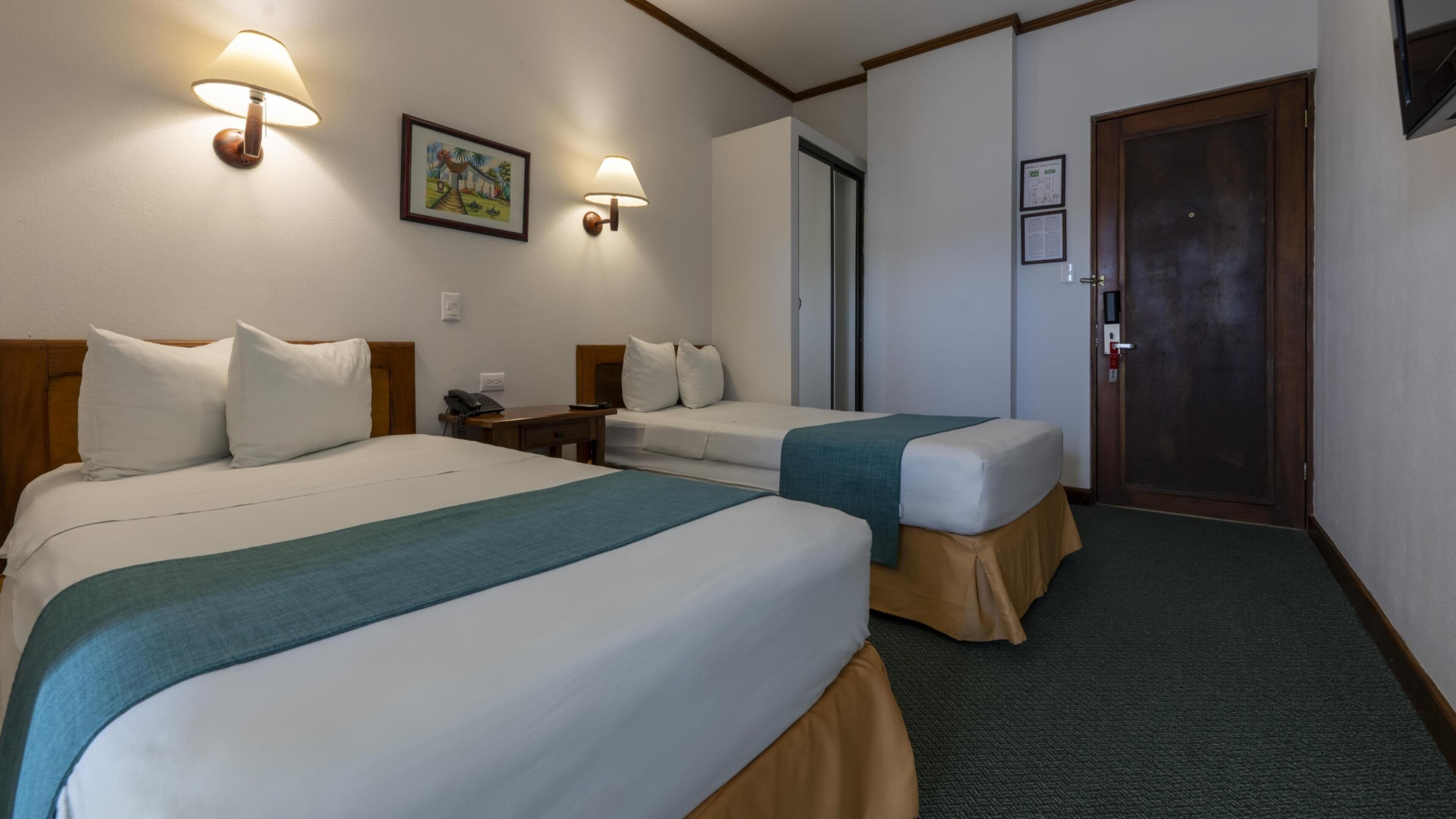 A hotel room with two beds, a desk, a chair, a phone, and a door.