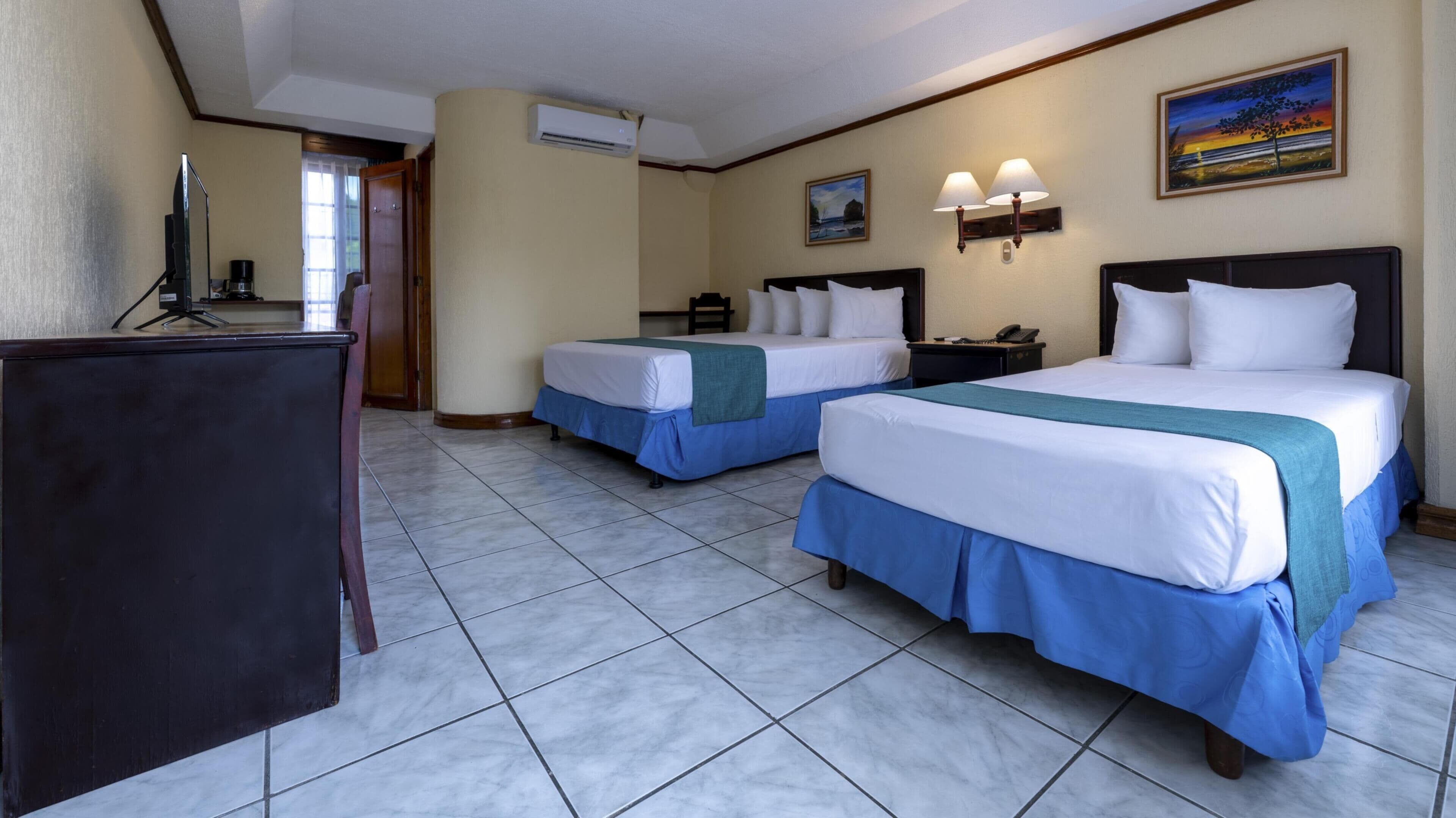 Habitación de hotel con dos camas, un escritorio y un televisor.