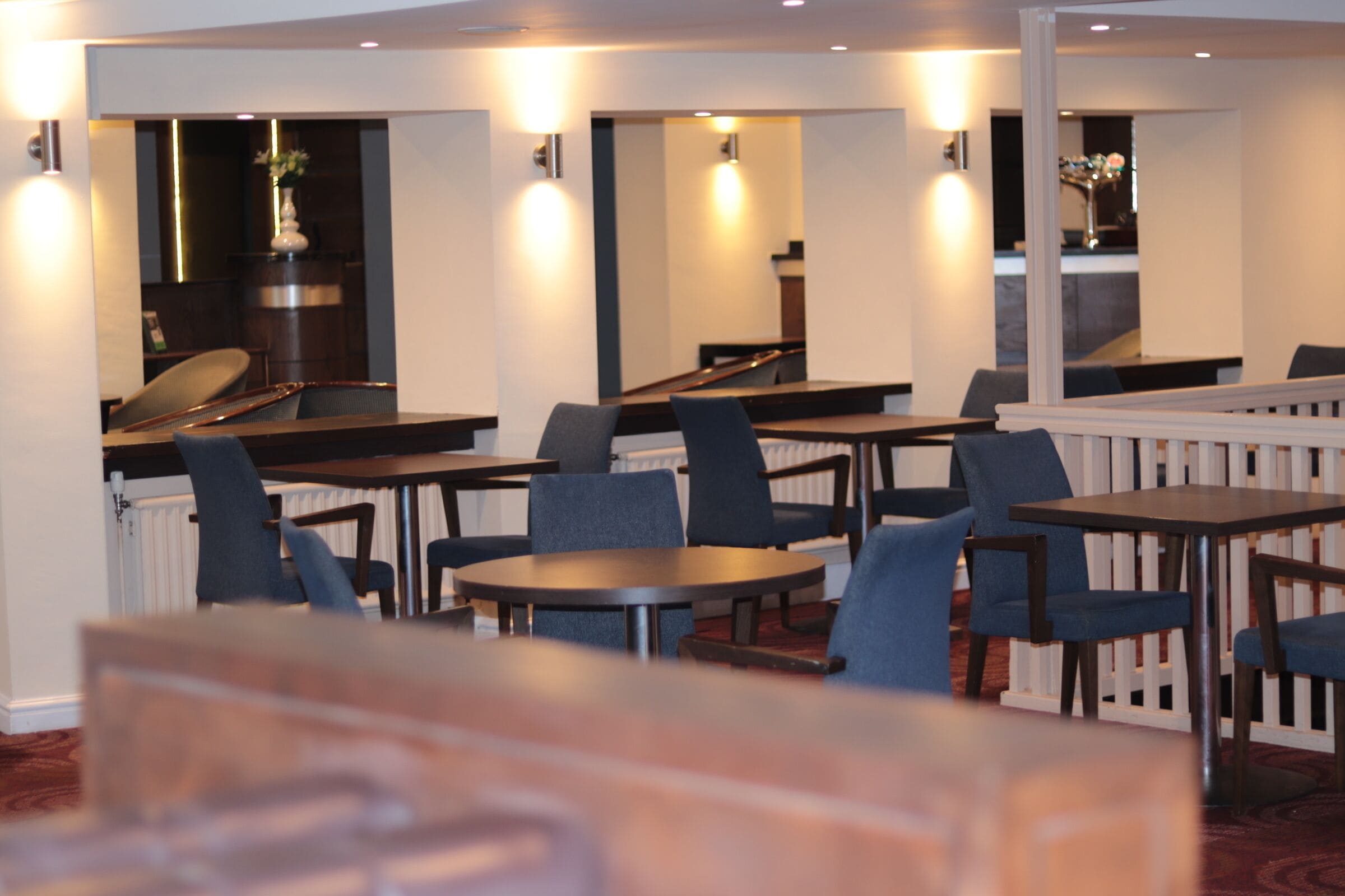 A restaurant with multiple tables and chairs, a counter, and a staircase leading to an upper level.