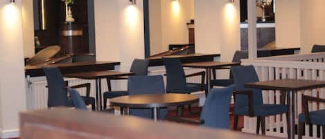 A restaurant with multiple tables and chairs, a counter, and a staircase leading to an upper level.