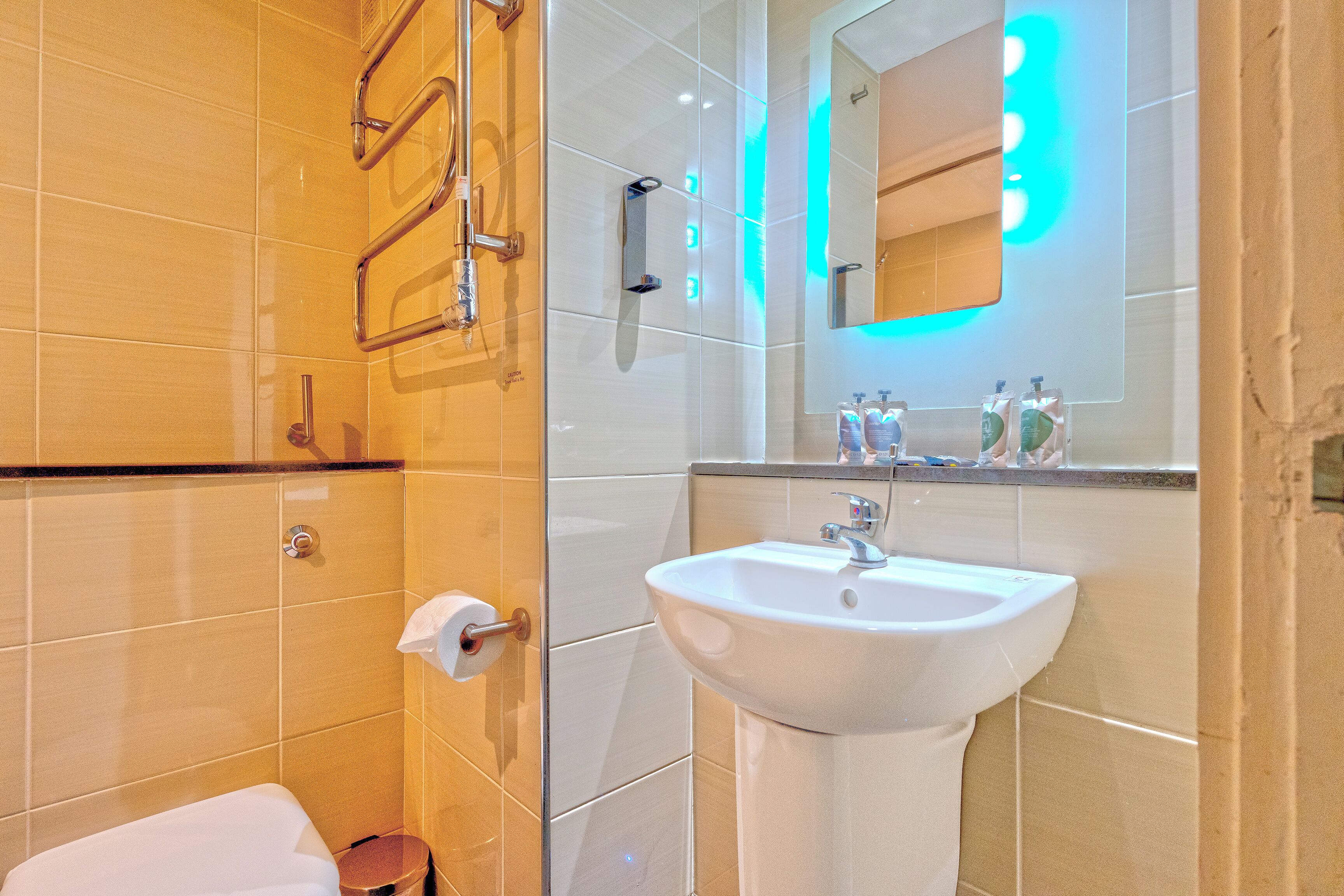 A bathroom with a white sink, a mirror with lights, and a towel rack.