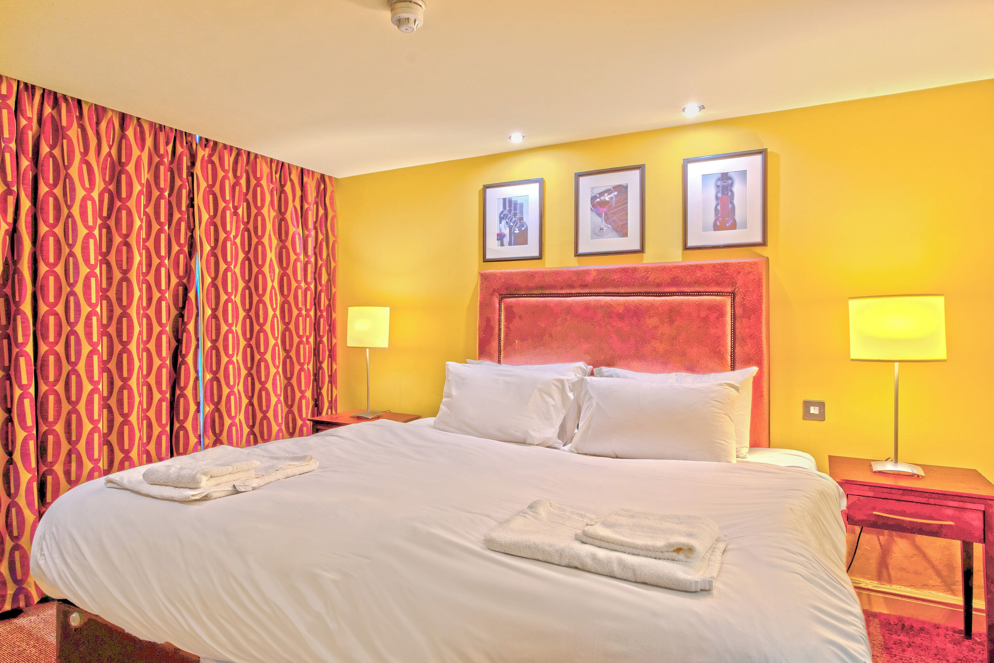 A hotel room with a large bed, two bedside lamps, and a red curtain.