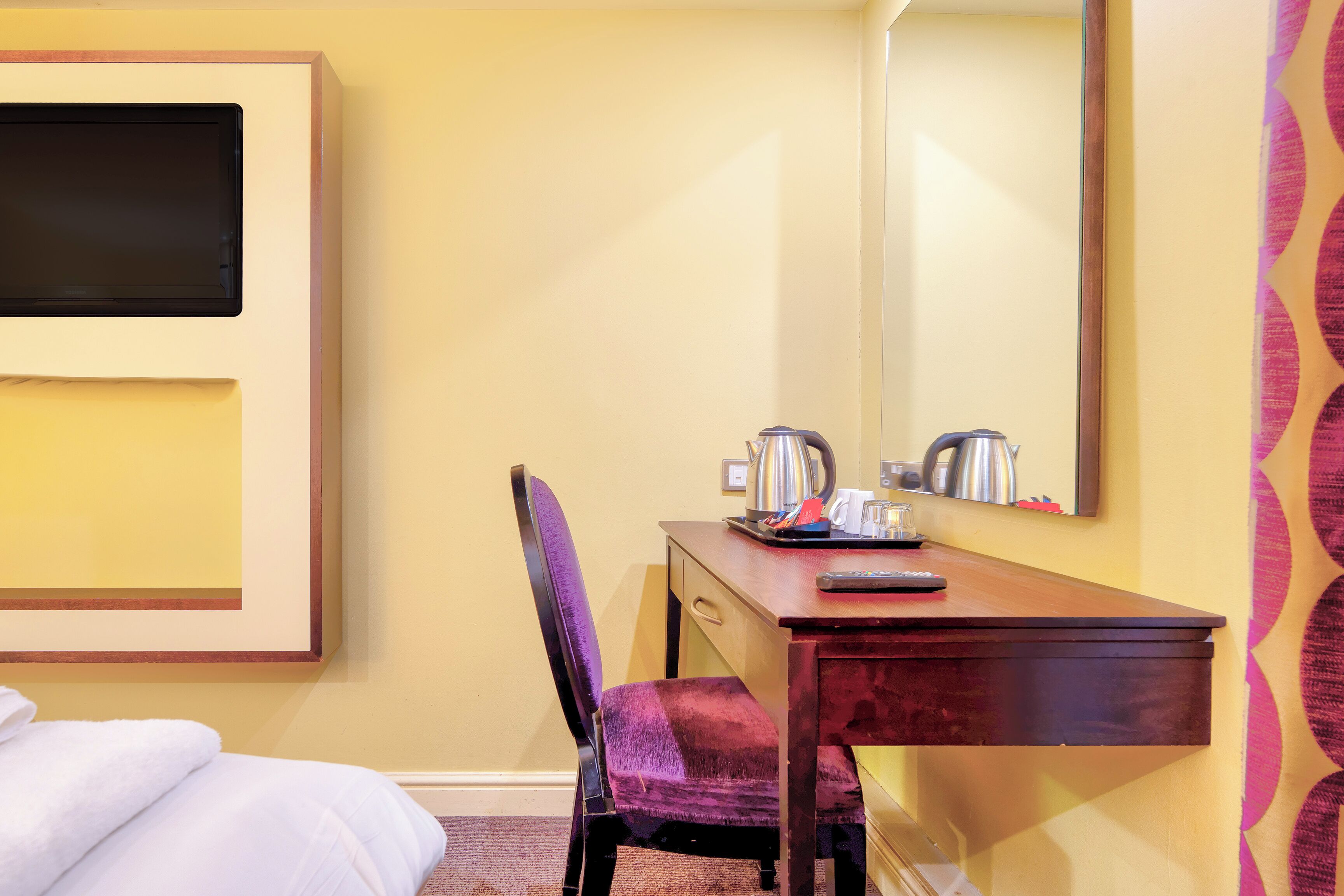 A hotel room with a bed, a desk with a chair, a coffee maker, and a mirror.