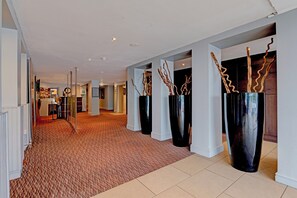 Un couloir d’hôtel avec un tapis à motifs, de grands vases noirs ornés de branches et un aménagement intérieur moderne.