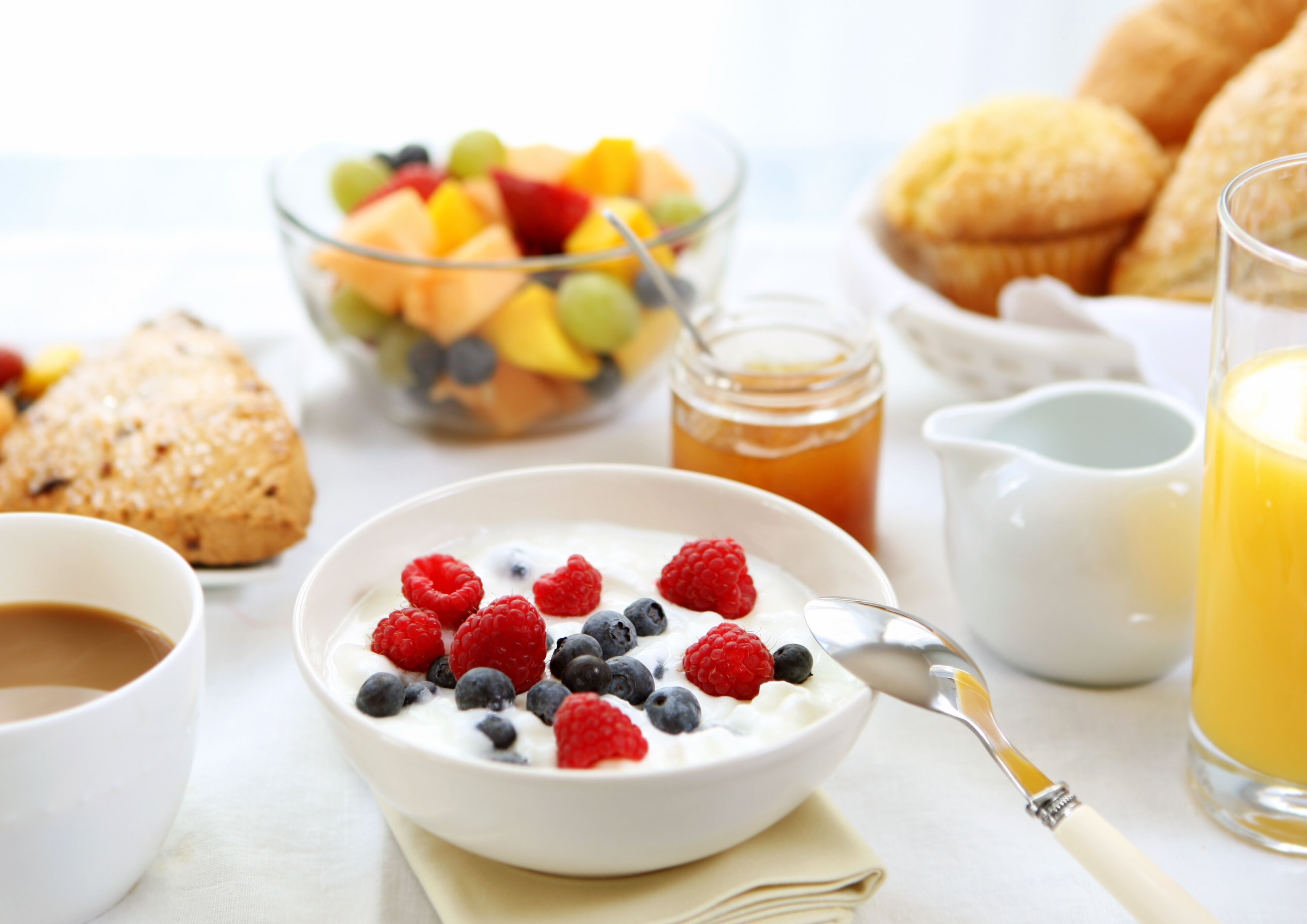A breakfast setting with a bowl of yogurt topped with berries, a glass of orange juice, and a jar of honey.