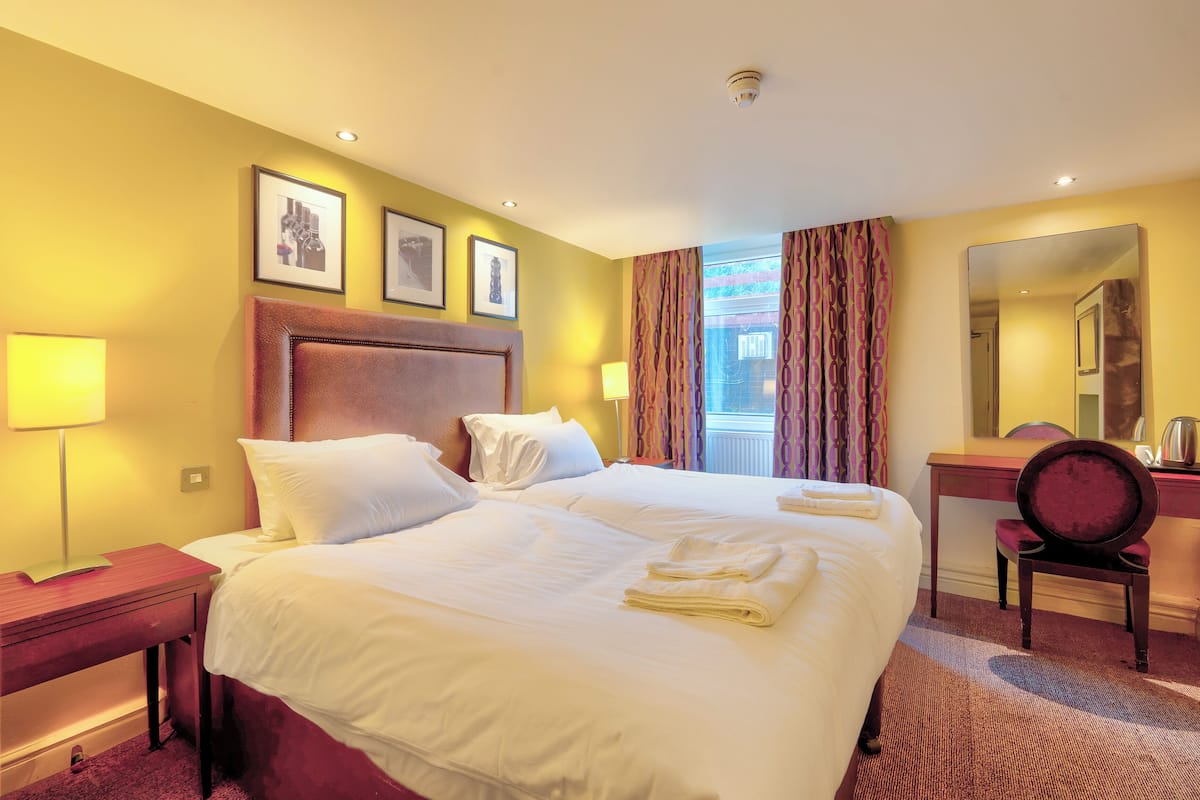 A hotel room with a large bed, a desk, a chair, and a mirror.