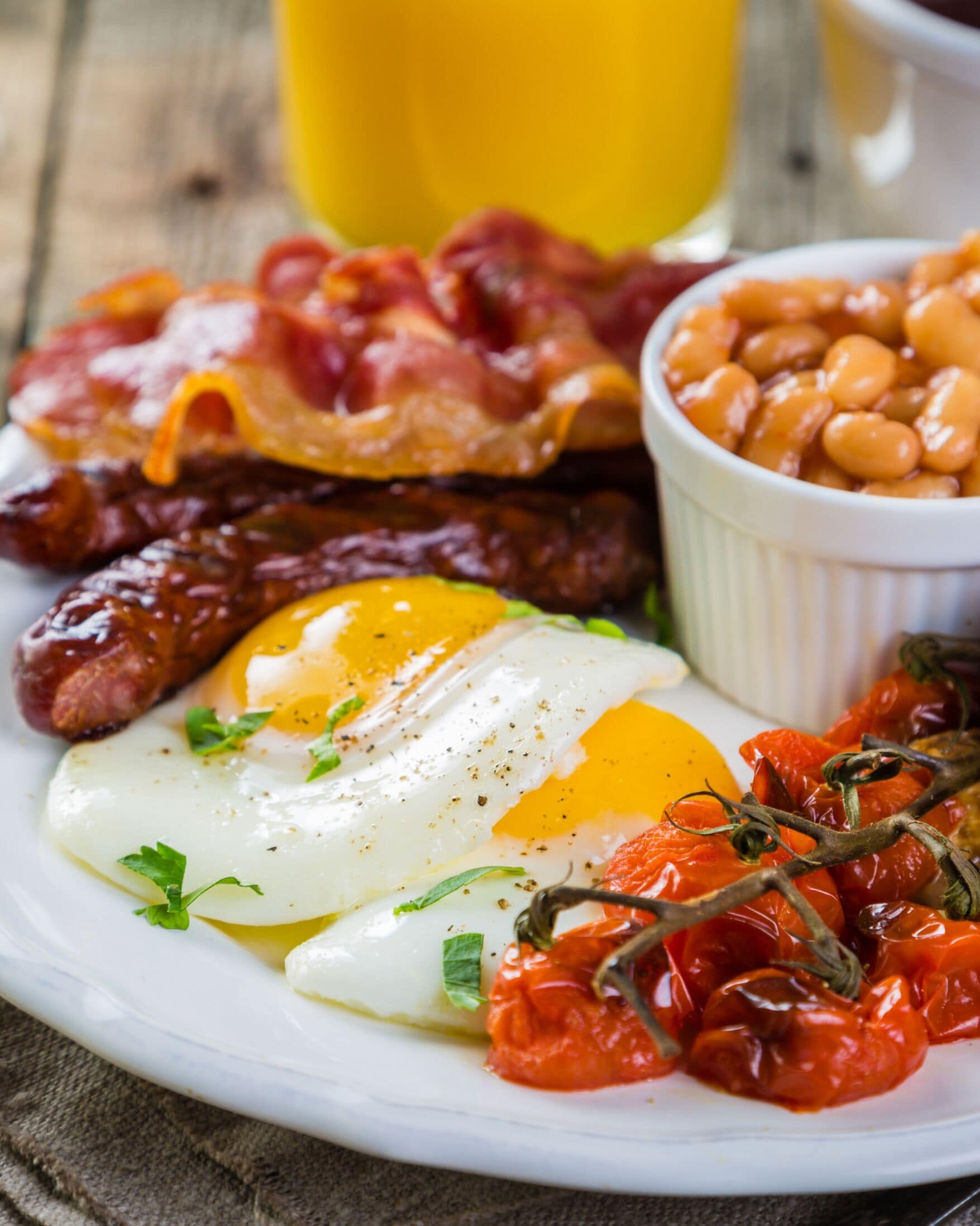 Un plato de desayuno con huevos, tocino, salchichas, frijoles y tomates.