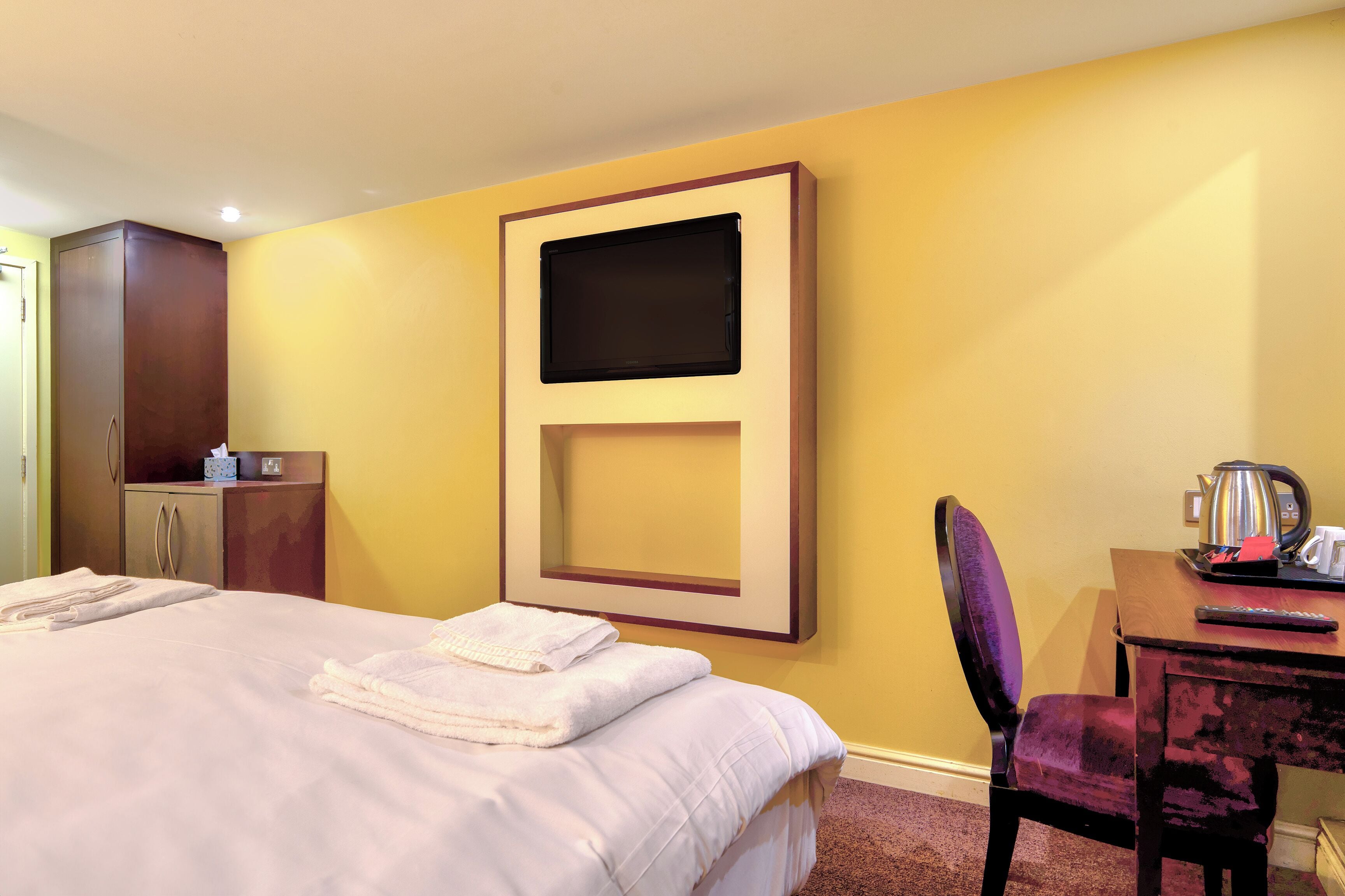 A hotel room with a bed, a desk, a chair, a television, and a wardrobe.