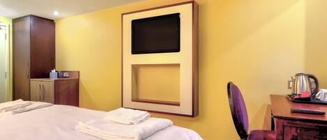 A hotel room with a bed, a desk, a chair, a television, and a wardrobe.
