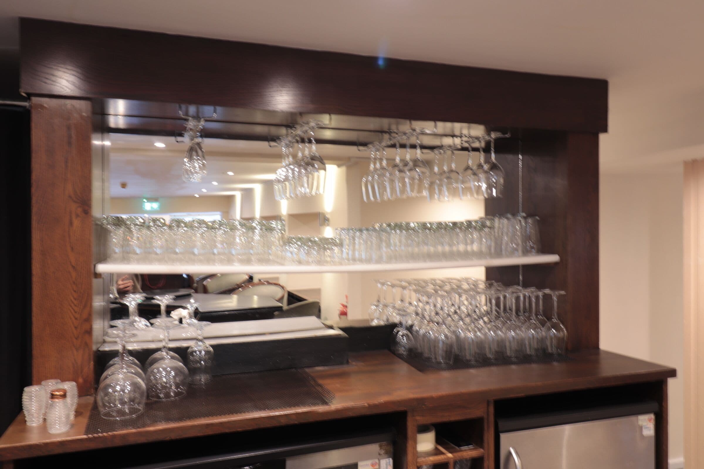 Zona de bar con estanterías llenas de vasos y un enfriador de vino.