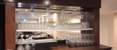 Zona de bar con estanterías llenas de vasos y un enfriador de vino.