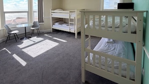 A hotel room with bunk beds, a small table with chairs, a window with a view, and a TV on the upper bunk.