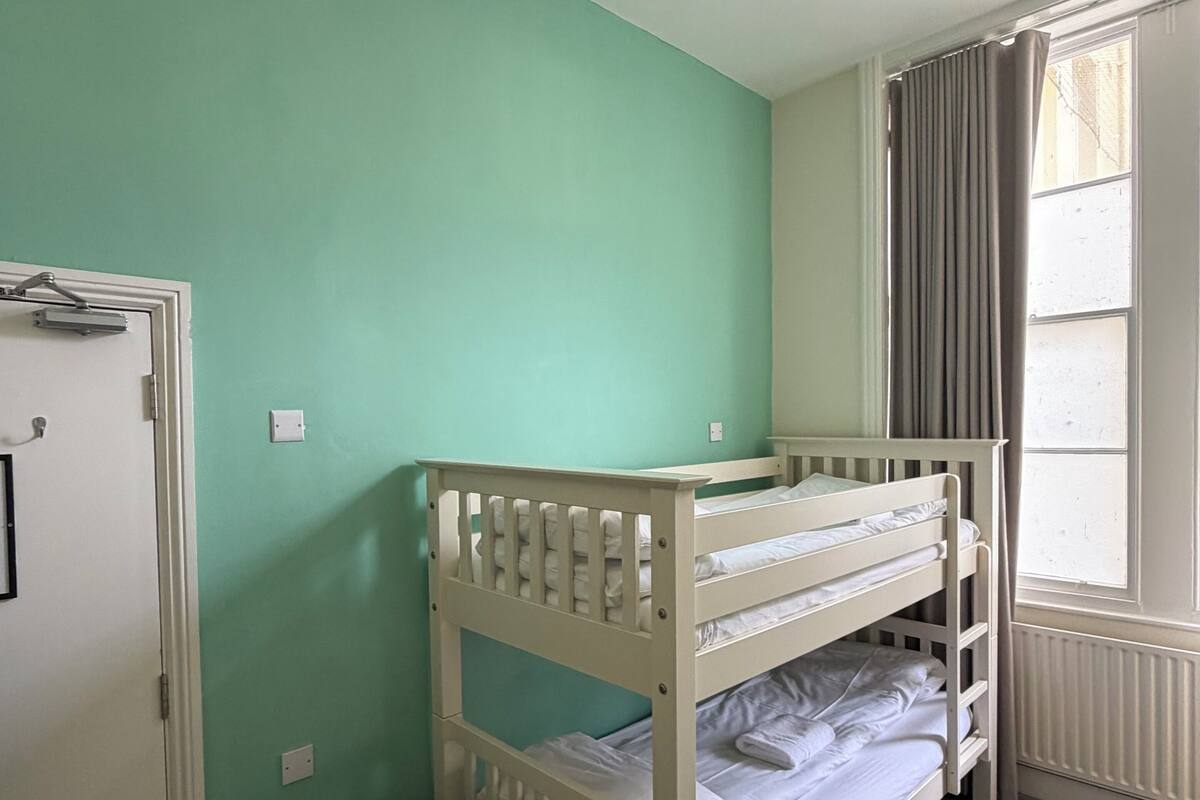 A room with a bunk bed, a door, a radiator, and a window with curtains.
