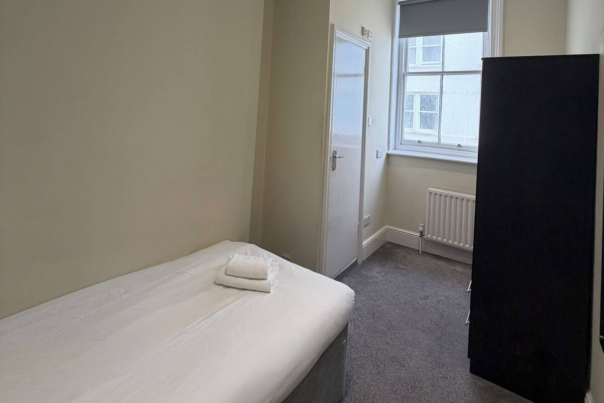 A bedroom with a single bed, a door, a radiator, and a window.