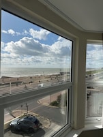 A view from a window overlooking a coastal road with a beach, a roundabout, and a car parked on the street.