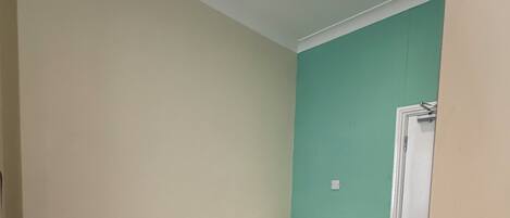 A small, single-bed room with a grey carpet, a white mattress, and a teal accent wall.