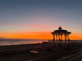 Um gazebo com arquitetura elaborada, vista para a água e mar tranquilo ao pôr do sol.