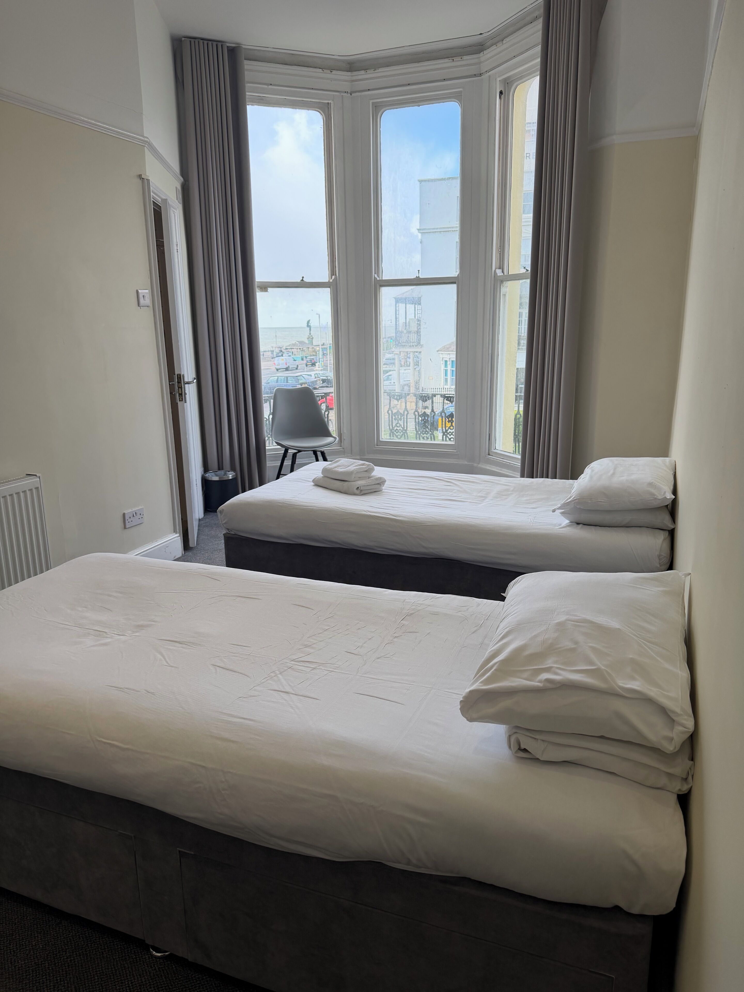 A hotel room with two beds, a chair, and a view of the city through large windows.