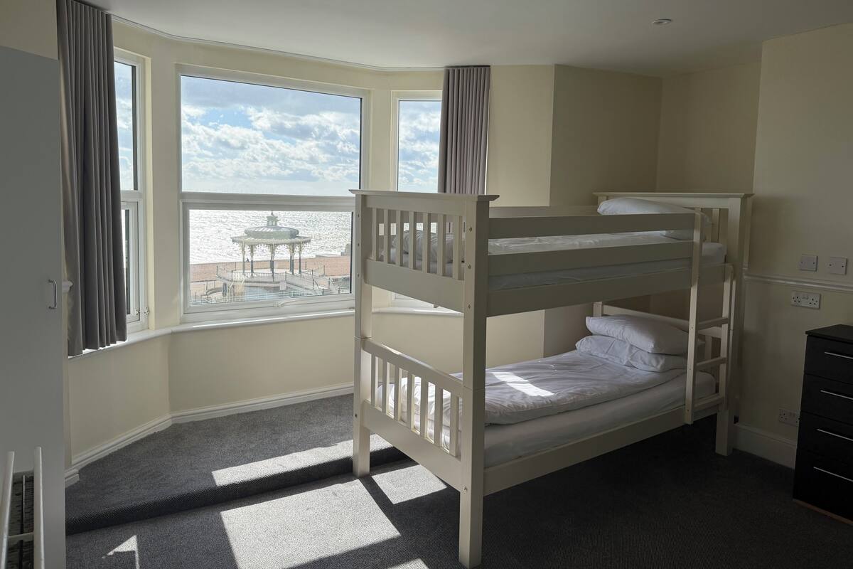 A bunk bed room with large windows, a view of a gazebo, and a small table outside.