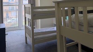 A hotel room with bunk beds, a desk, and a large window with a view of buildings.