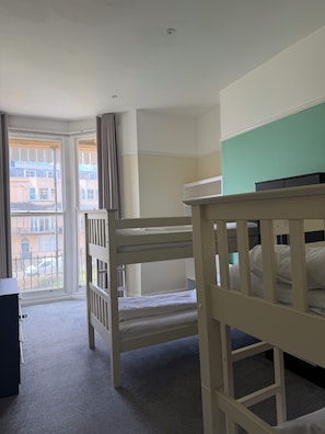 A hotel room with bunk beds, a desk, and a large window with a view of buildings. - The Brighton Hotel (Brighton)