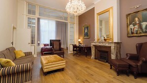 Uma sala de estar espaçosa, com um candelabro, lareira e móveis clássicos.