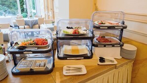 Buffet com diversos alimentos em recipientes transparentes, incluindo saladas, frutas e carnes.