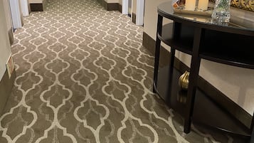 A hotel hallway with patterned carpet, a table with a vase, and a mirror on the wall.