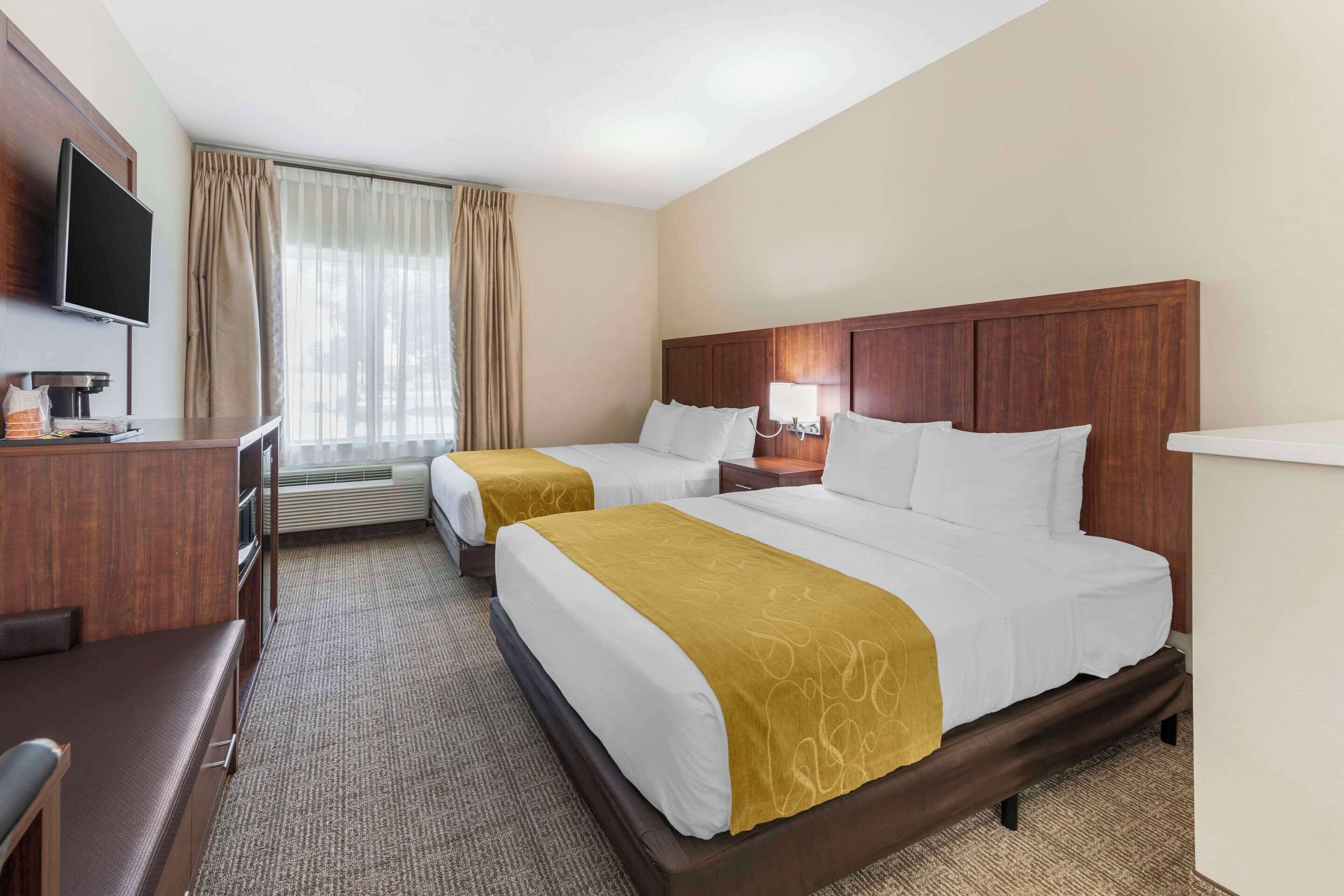 A hotel room with two beds, a desk, a TV, and a window with curtains.