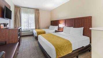 A hotel room with two beds, a desk, a TV, and a window with curtains.