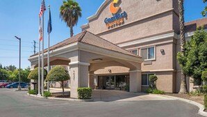 Un hotel Comfort Suites con fachada color beige, una entrada cubierta y palmeras.