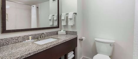 A bathroom with a granite countertop sink, a mirror, a toilet, and a towel rack.