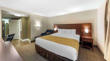 Une chambre d’hôtel avec un grand lit, un bureau, une chaise et une table de chevet avec une lampe.