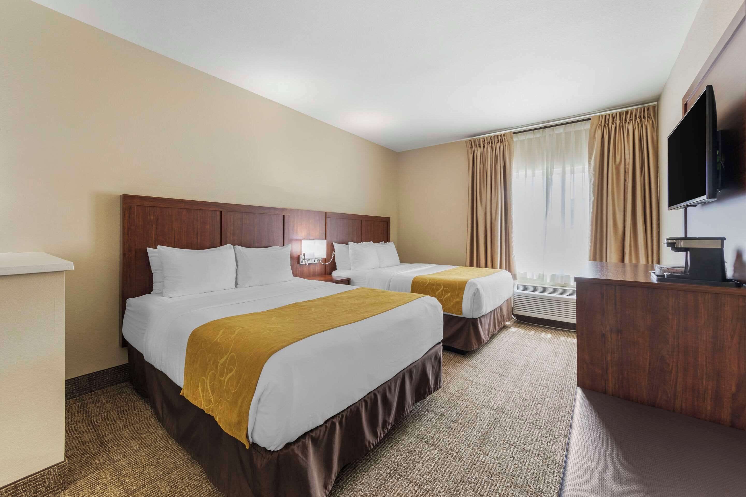 A hotel room with two beds, a desk, a television, and a window with curtains.