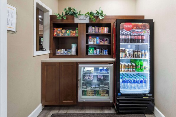 A vending machine with a Coca-Cola refrigerator, a mini-fridge, and shelves stocked with snacks and beverages. - Comfort Suites Tulare Sequoia Gateway (Tulare)