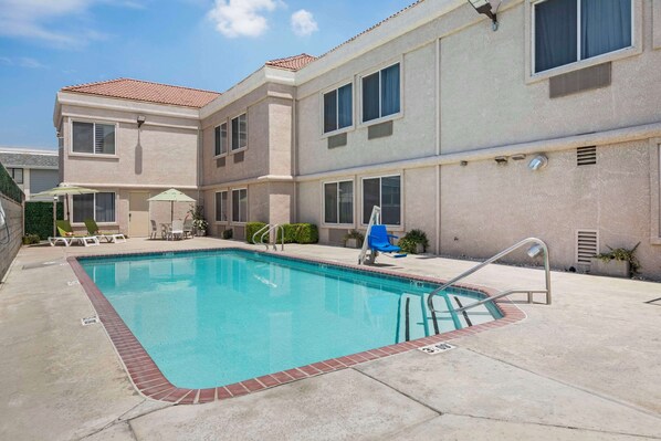 A swimming pool with a brick border, surrounded by a patio area with lounge chairs and umbrellas. - Comfort Suites Tulare Sequoia Gateway (Tulare)