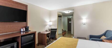 Une chambre d’hôtel comprenant un lit, un bureau avec une chaise, un petit réfrigérateur, une télévision et un miroir.