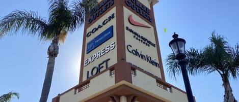 A multi-level tower with various brand names displayed on its facade, including Coach, Express, Calvin Klein, and others.