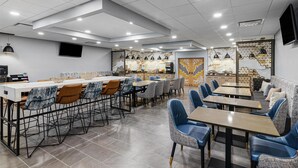 A modern dining area with multiple tables and chairs, a flat-screen TV mounted on the wall, and decorative wall art. - Best Western Plus Savannah Gateway (Savannah)