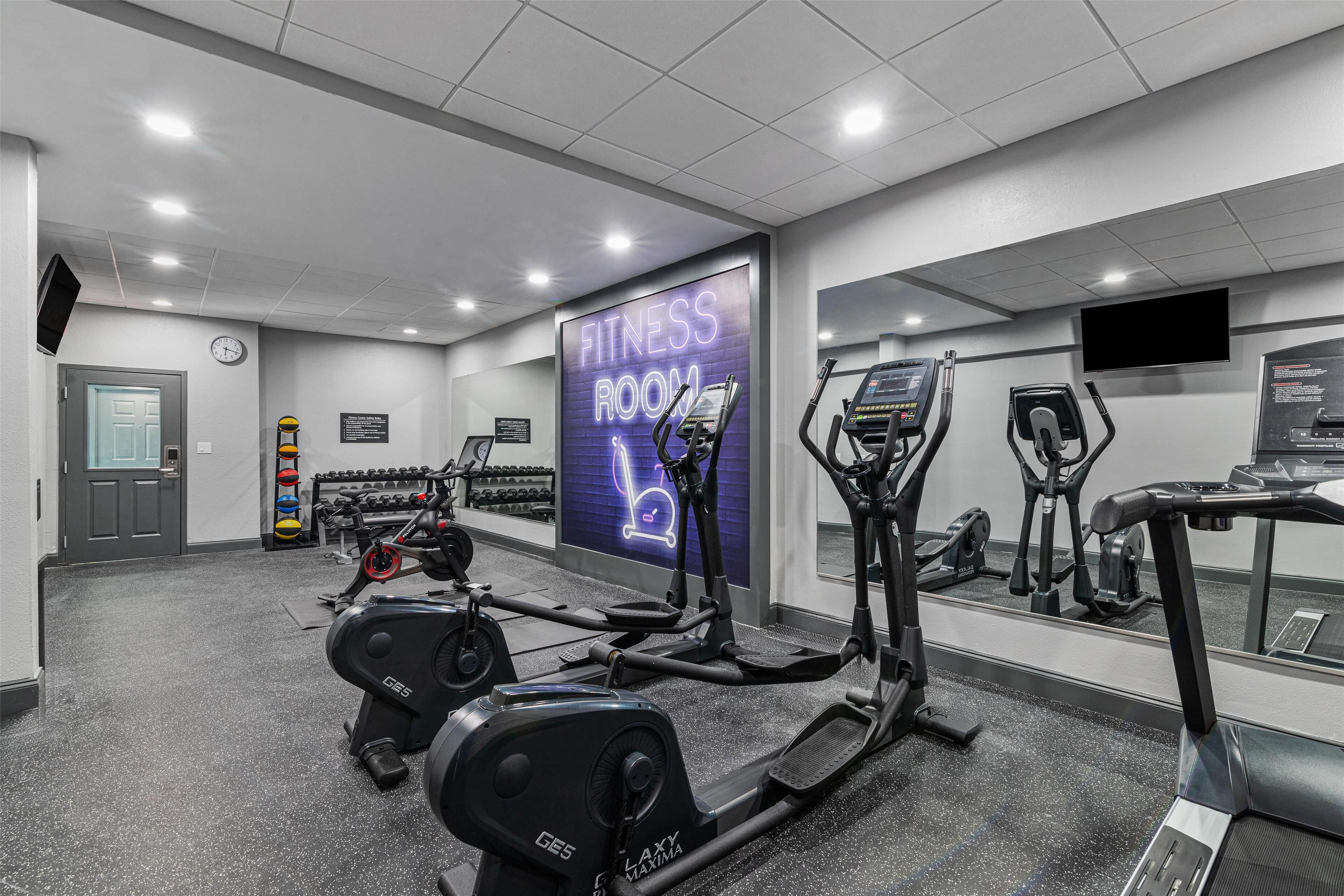 A fitness room with treadmills, elliptical machines, and a mirrored wall.