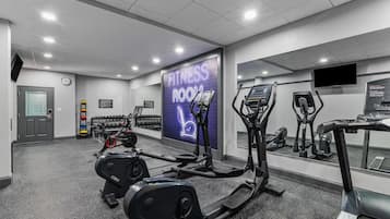 Uma sala de ginástica com esteiras, elípticos e um espelho grande.